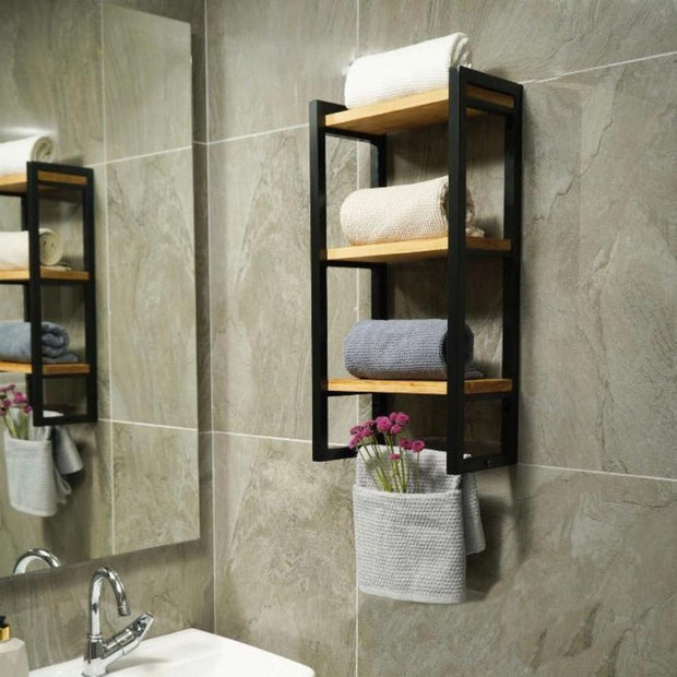 Wall-mounted three-shelf bathroom towel holder with wooden shelves and a black metal frame, neatly organizing towels and featuring a small hanging basket with flowers, placed against a gray tiled bathroom wall.