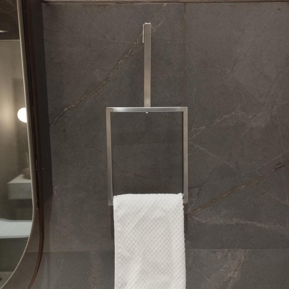 A minimalist vertical towel ring in a satin nickel finish is mounted on a dark stone wall. The sleek, rectangular design holds a white textured towel, adding a modern touch to the bathroom decor. The towel ring's simple yet elegant design complements the sophisticated ambiance of the space.