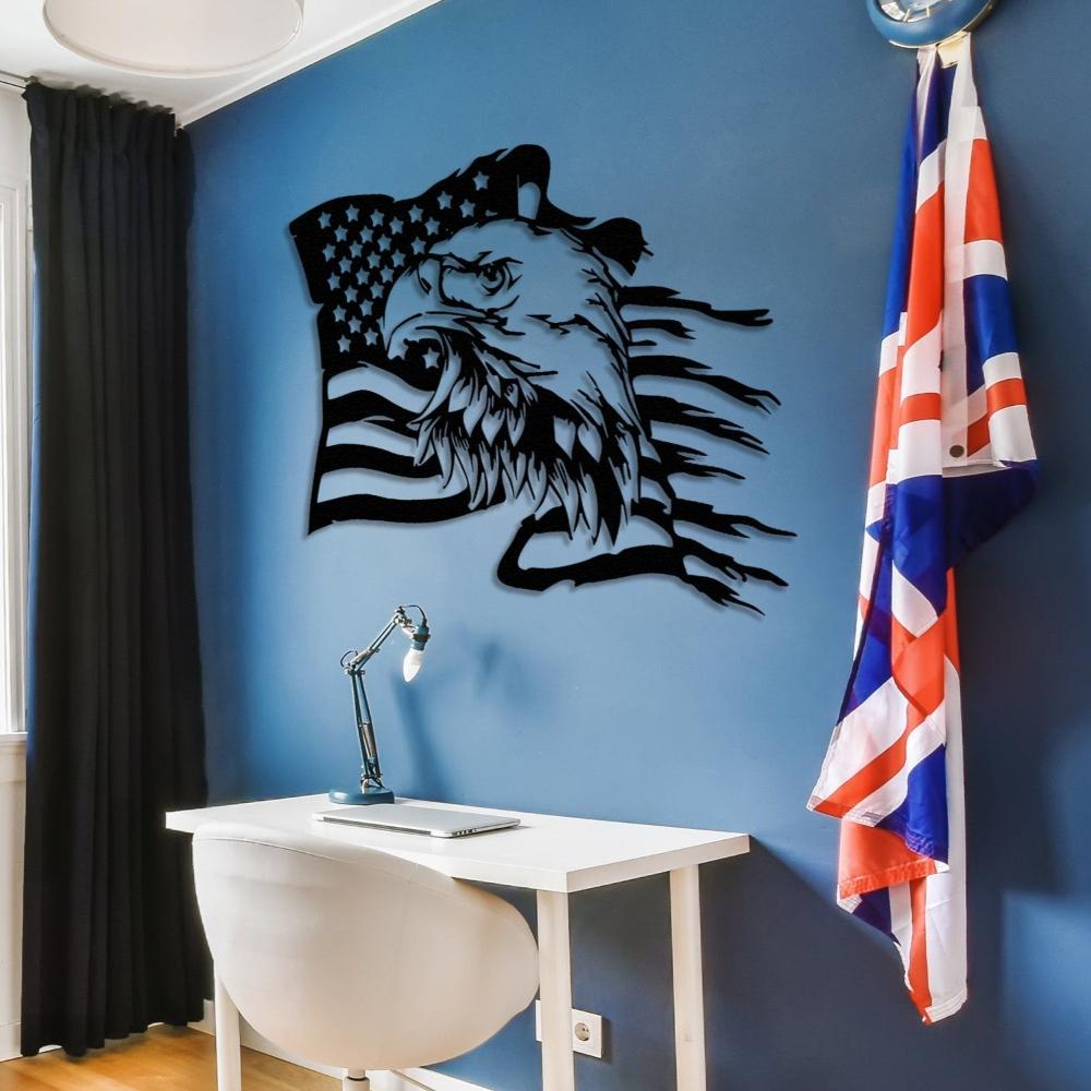 Black metal wall art of an American flag with a fierce eagle head design mounted on a blue wall, accompanied by a white desk and chair, with a flag draped in the corner.