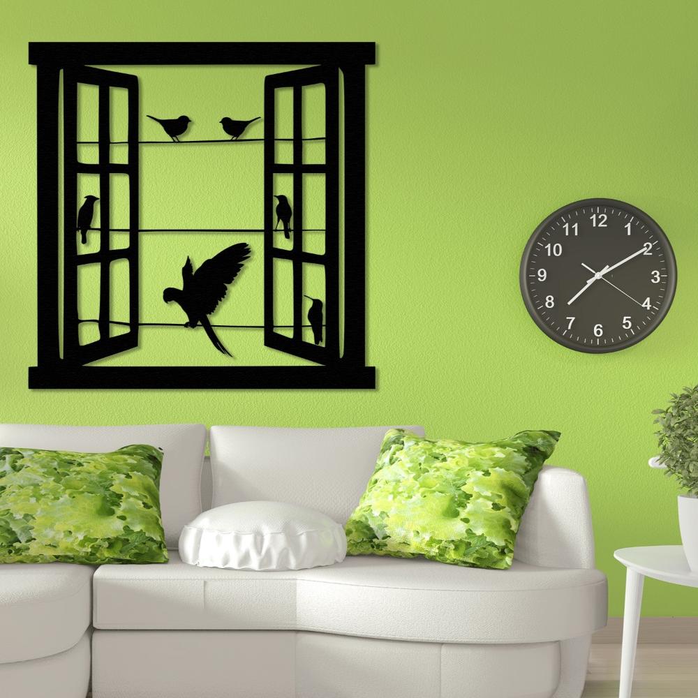 Black metal wall art featuring an open window with bird silhouettes perched on wires and a flying parrot in the center, mounted on a lime green wall above a white couch with green floral-patterned cushions and a black wall clock.