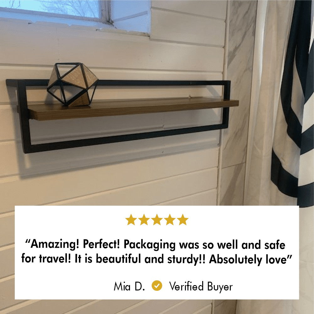 A wooden and black metal bathroom shelf with a geometric decoration on top, accompanied by a customer review stating "Amazing! Perfect! Packaging was so well and safe for travel! It is beautiful and sturdy!! Absolutely love" by Mia D.