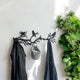 A black metal wall-mounted coat rack designed with birds perched on tree branches. It features hooks for hanging coats, hats, or scarves, blending functionality with a nature-inspired decorative element. The rack is positioned against a white wall, with a leafy green plant nearby, creating a fresh and modern look for any entryway or living space.