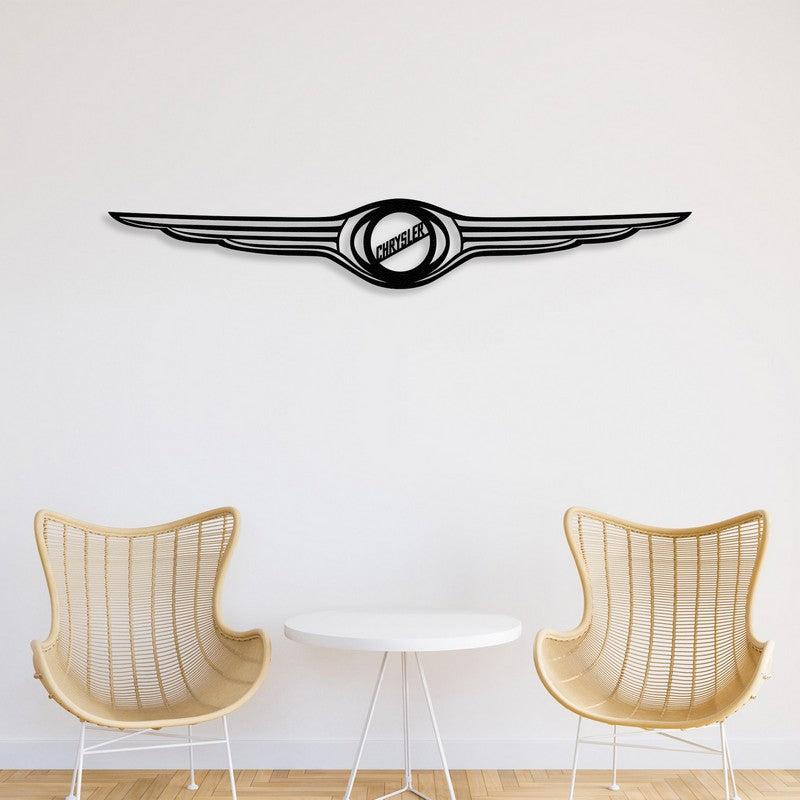 A sleek black Chrysler-inspired metal wall art with a winged design, mounted on a clean white wall. Below, two modern wicker chairs and a minimalist white round table create a stylish and contemporary setting.