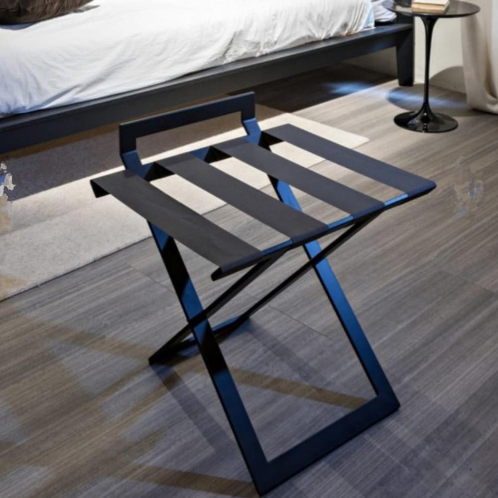 A black foldable luggage rack with leather straps placed under soft lighting in a modern bedroom, highlighting its sturdy build and premium material.