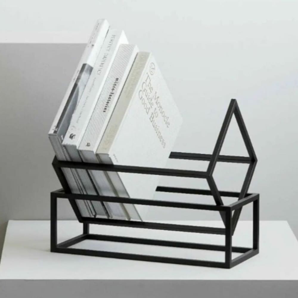 A black geometric book rack on a white pedestal, holding a selection of monochromatic books with a modern minimalist style