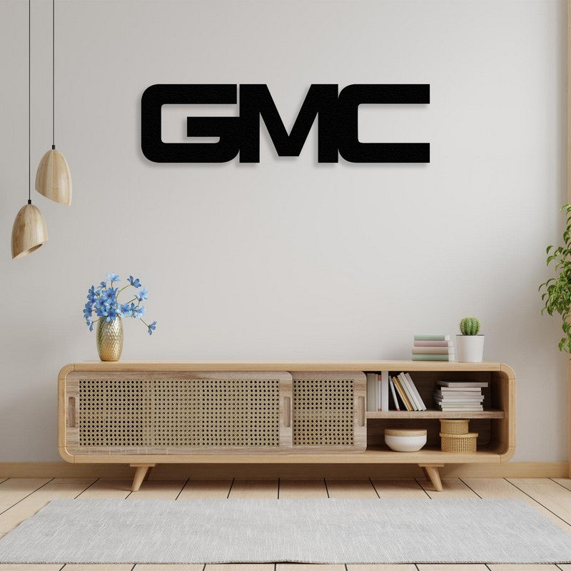 GMC-themed black metal wall art displayed above a modern wooden console table with cane doors, adorned with a vase of blue flowers and surrounded by minimalist decor in a bright living space.