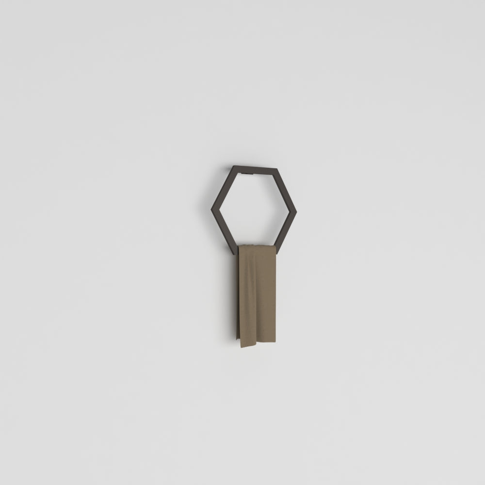 Black hexagon-shaped towel ring mounted on a plain white wall, holding a beige towel, showcasing minimalist bathroom decor.