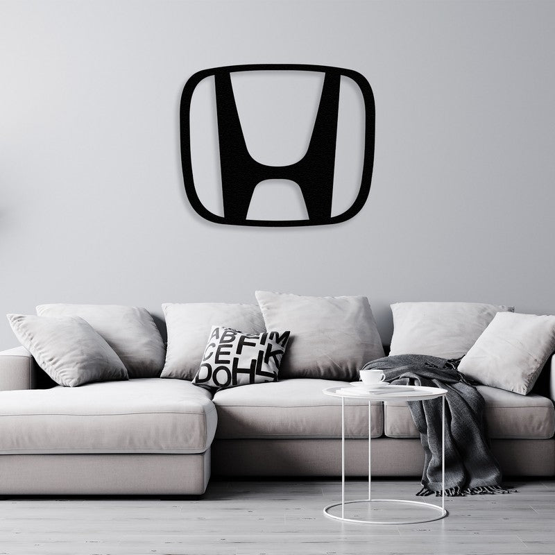 A modern black Honda-inspired metal wall art centerpiece displayed above a light gray sectional sofa with minimalist decor, including monochromatic throw pillows and a small white side table with a cozy throw.