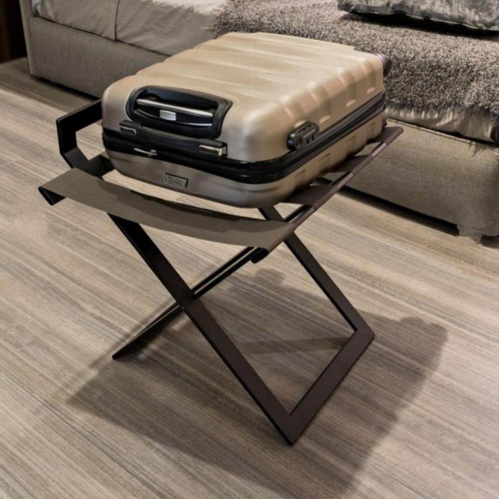 A foldable black luggage rack with wide leather straps holding a beige suitcase, demonstrating its practicality for guest room use on a sleek bedroom floor