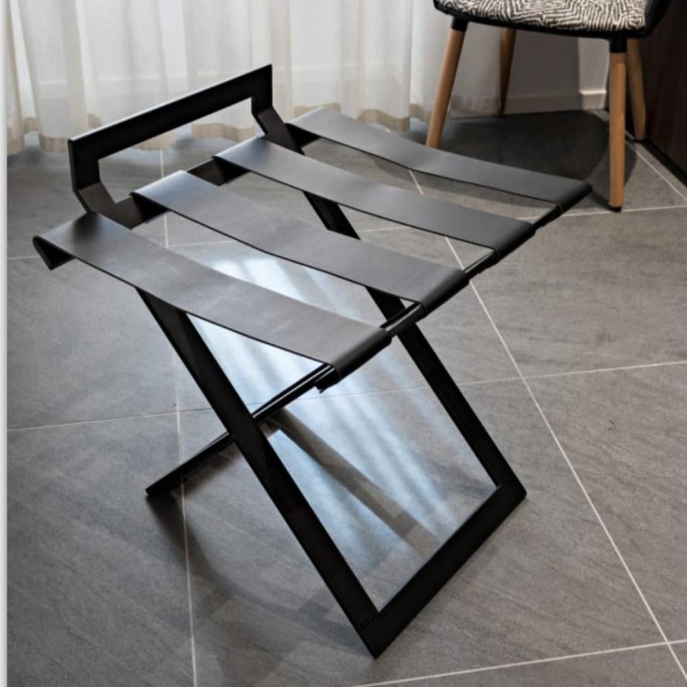 A detailed view of a black luggage rack’s straps and frame, focusing on its minimalist design and robust construction on a tiled floor