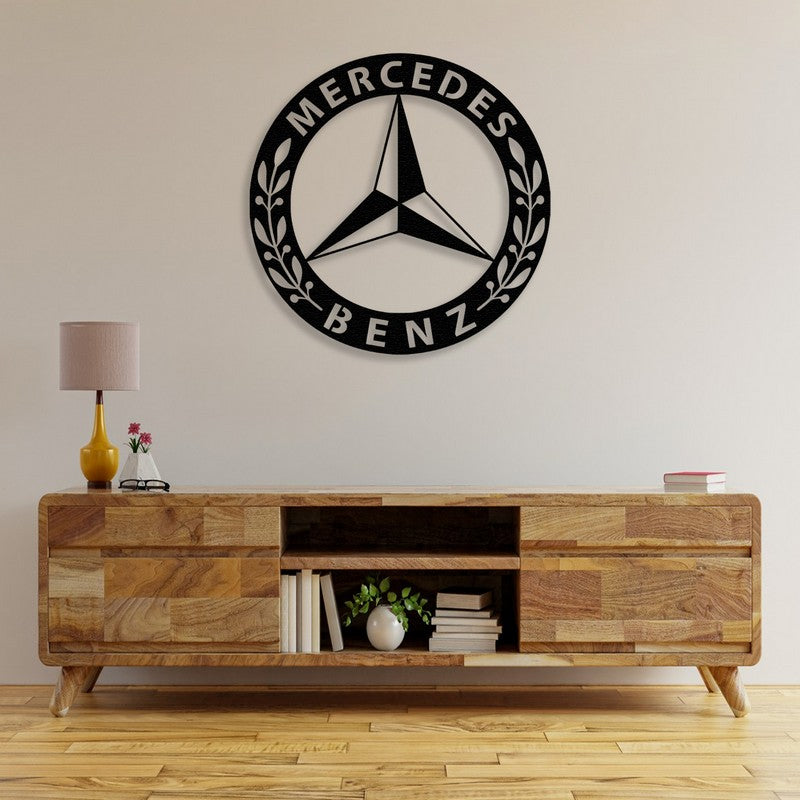 A sophisticated black Mercedes-Benz-inspired metal wall art displayed above a rustic wooden console table adorned with books, a small plant, and a yellow lamp, creating a refined and timeless decor.