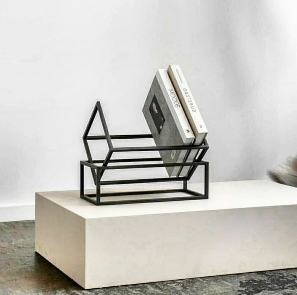 A black metal book holder displayed on a white pedestal, showcasing its angular geometric design and two books