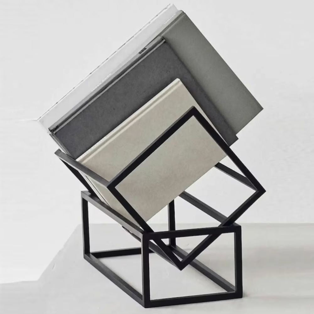 A modern black metal book rack holding a stack of books with a minimalist design, placed on a white surface