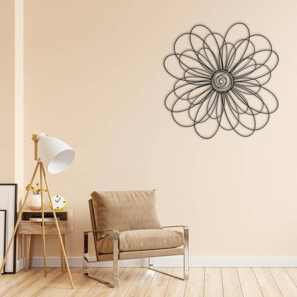 Black metal daisy wall art with intricate loops displayed on a beige wall above a cozy chair and a wooden side table in a modern living space.