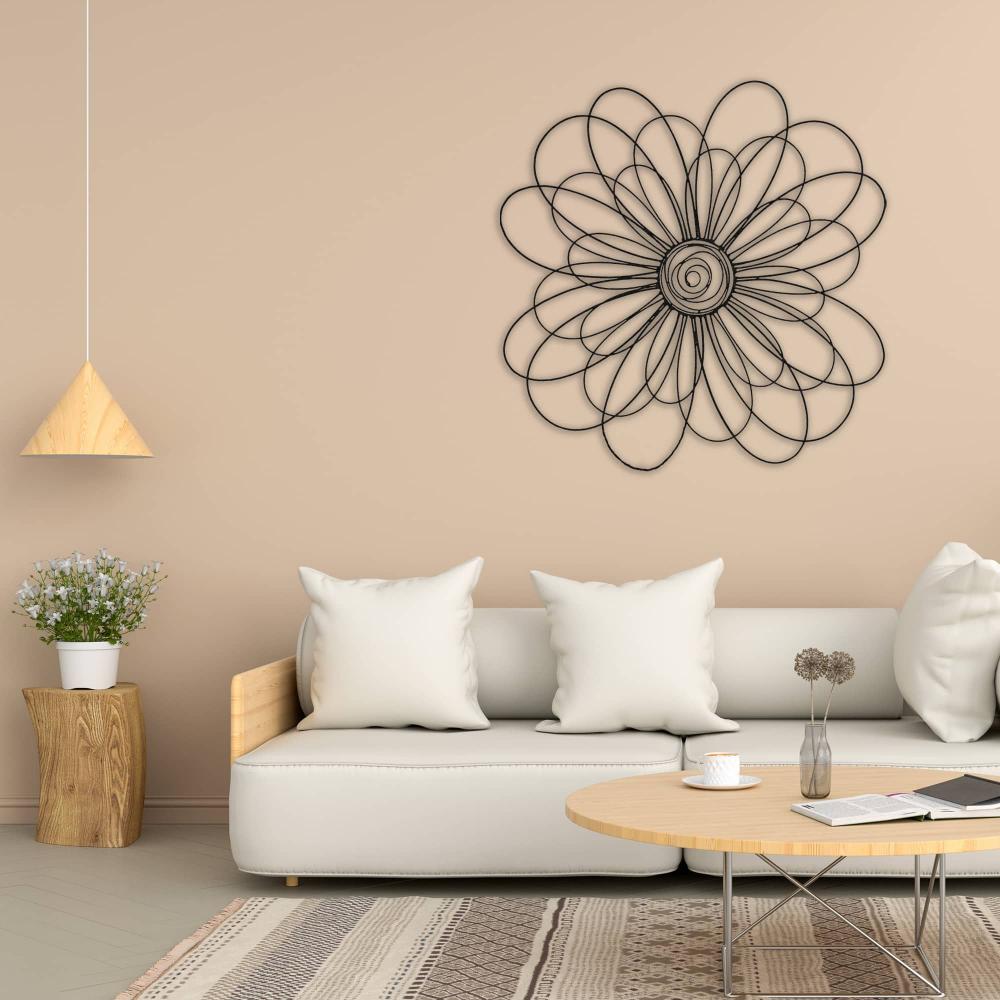 Black metal daisy wall art with a detailed spiral center displayed on a beige wall above a modern cream sofa, styled with white pillows and a wooden coffee table.