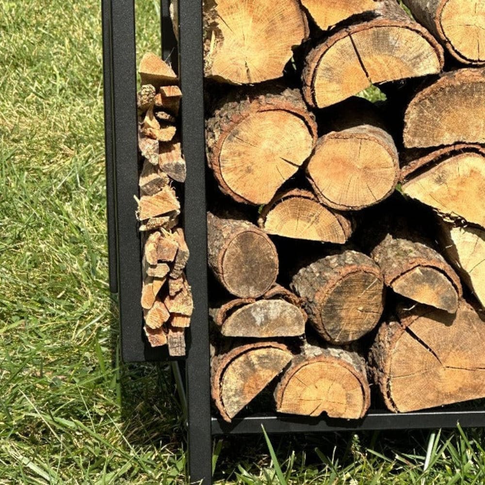 Close-up view of firewood stacked inside a black metal firewood holder, placed on a green lawn