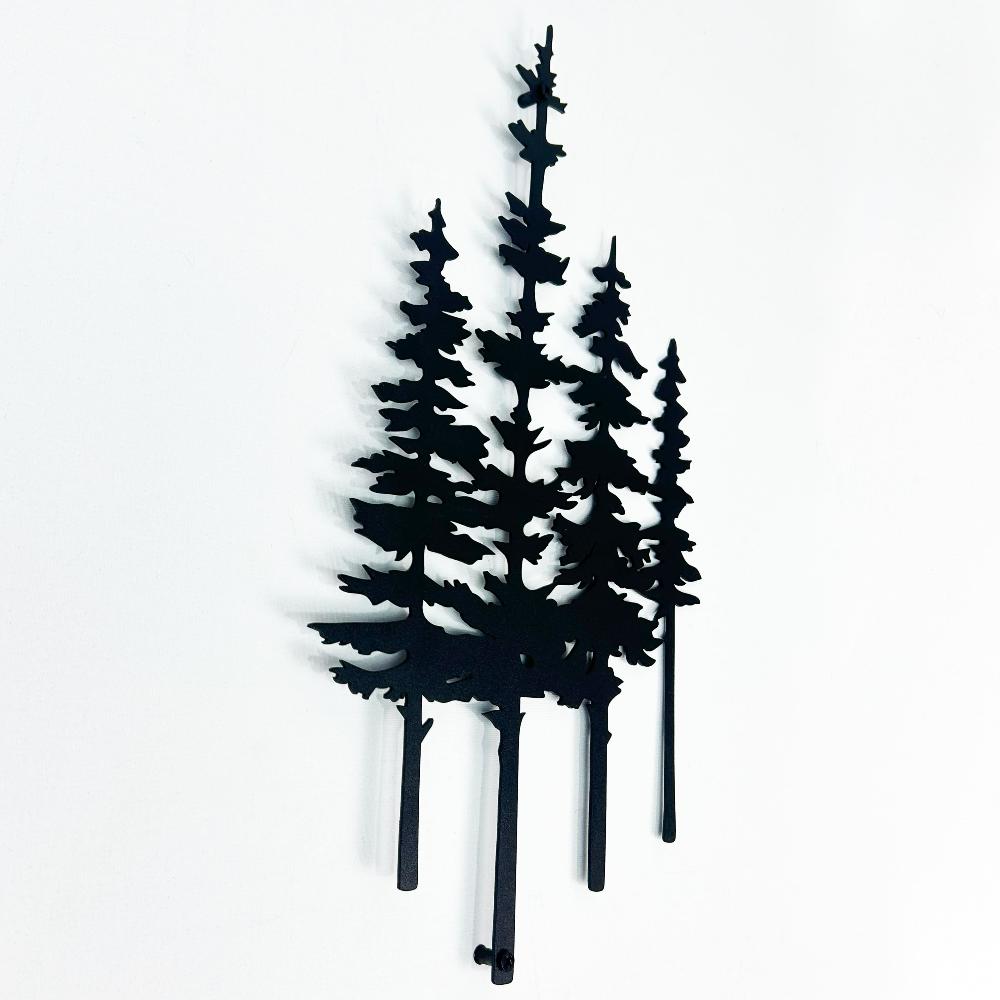 Close-up view of a black metal pine tree wall art piece showcasing intricate tree silhouettes against a white background.