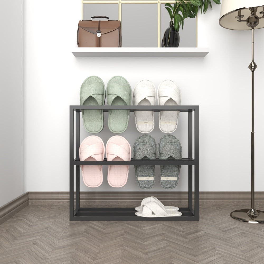 Front view of a simple black metal slipper rack, displayed with two pairs of white and green slippers against a plain white background for a minimalist aesthetic