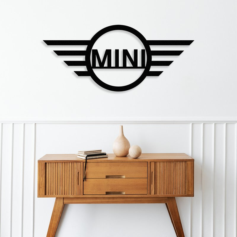 A sleek black metal wall art with a Mini-Cooper inspired design mounted above a mid-century modern wooden console table, adorned with minimalist decor items including books and ceramic vases, against a bright white wall with subtle paneling.