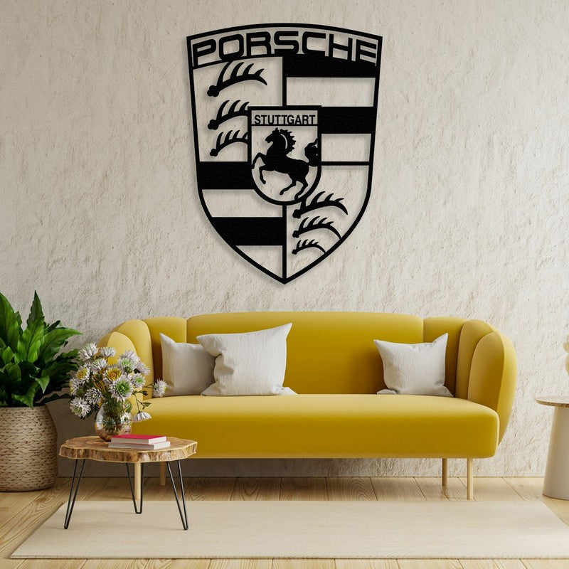 Black metal Porsche emblem wall art featuring intricate designs, mounted on a textured beige wall above a vibrant yellow sofa. The room is adorned with a rustic wooden coffee table, fresh flowers, and indoor plants, creating a cozy yet stylish ambiance.