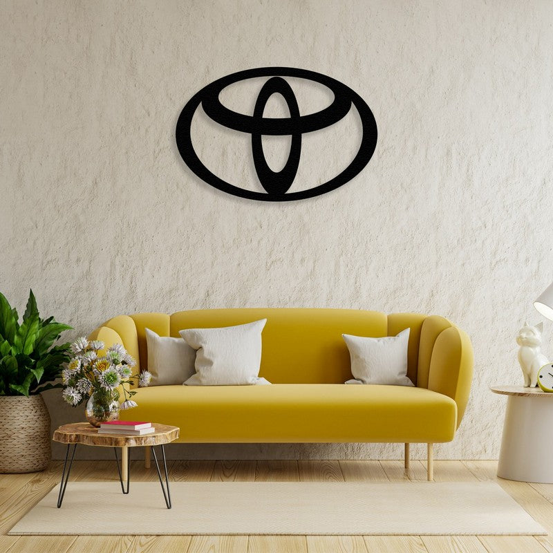 Black Toyota-inspired metal wall art mounted on a textured beige wall above a modern yellow sofa with white cushions, accompanied by a wooden coffee table and indoor plants.