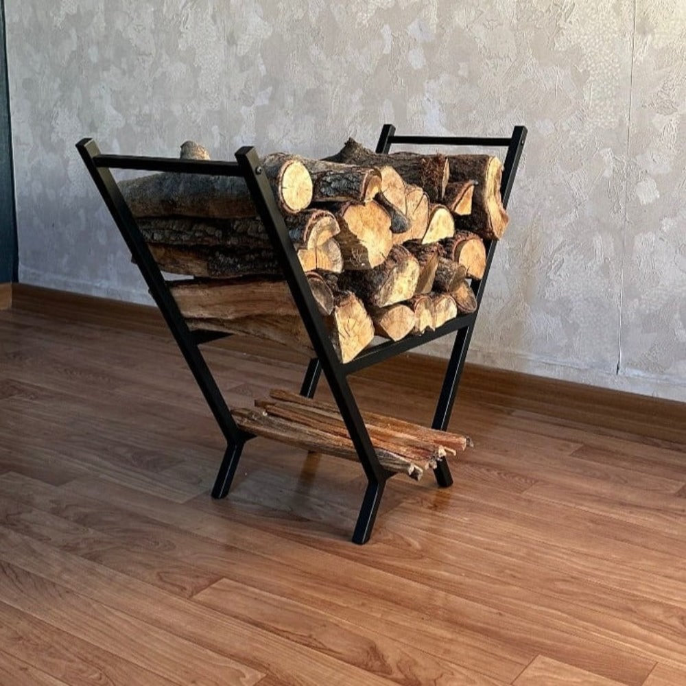 A black V-shaped metal wood rack fully loaded with firewood, displayed on wooden flooring with a textured wall in the background