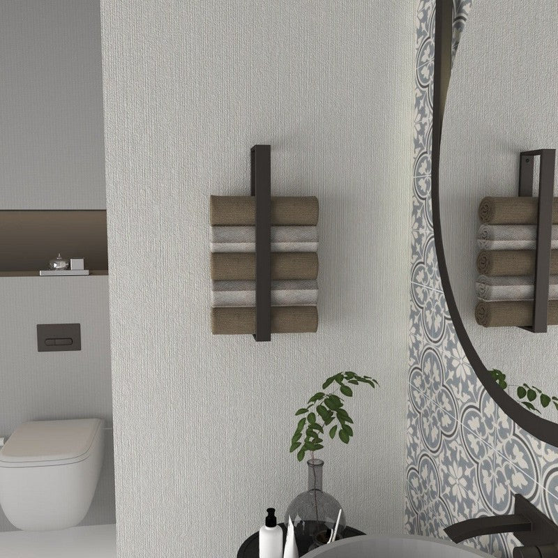 A minimalist black vertical towel rack mounted on a textured bathroom wall, holding rolled towels in shades of beige and gray. A circular mirror and decorative plants complement the modern design.