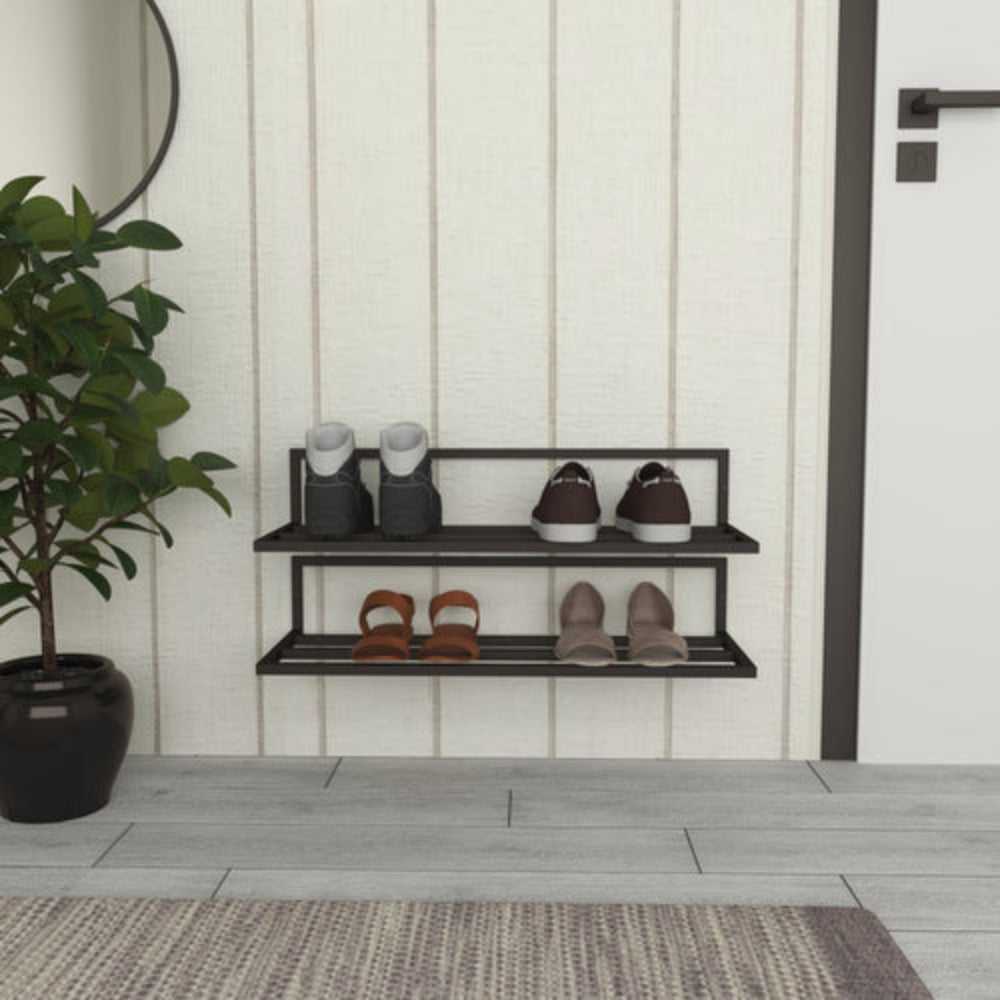 A black wall-mounted shoe rack with two tiers, showcasing boots, sneakers, and heels, located in an entryway with a potted plant, a circular mirror, and a beige paneled wall.