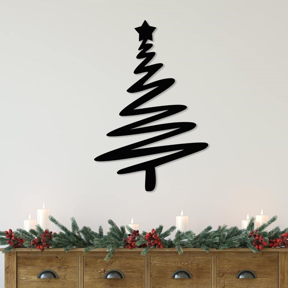 Black Christmas tree-shaped metal wall art with a star on top, mounted on a light wall above a rustic wooden dresser decorated with festive greenery, red berries, and candles.