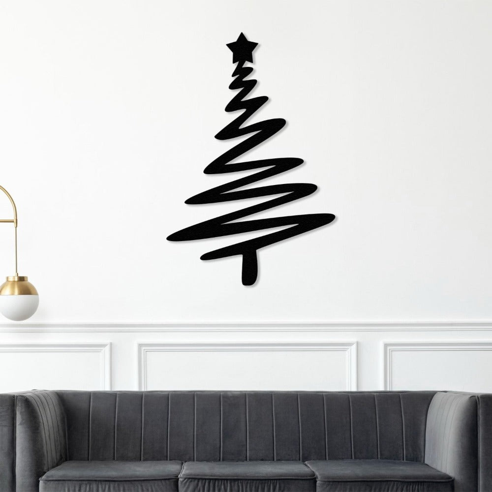 Black Christmas tree-shaped metal wall art with a star on top, mounted on a white wall above a modern gray sofa, with a gold-accented lamp nearby.