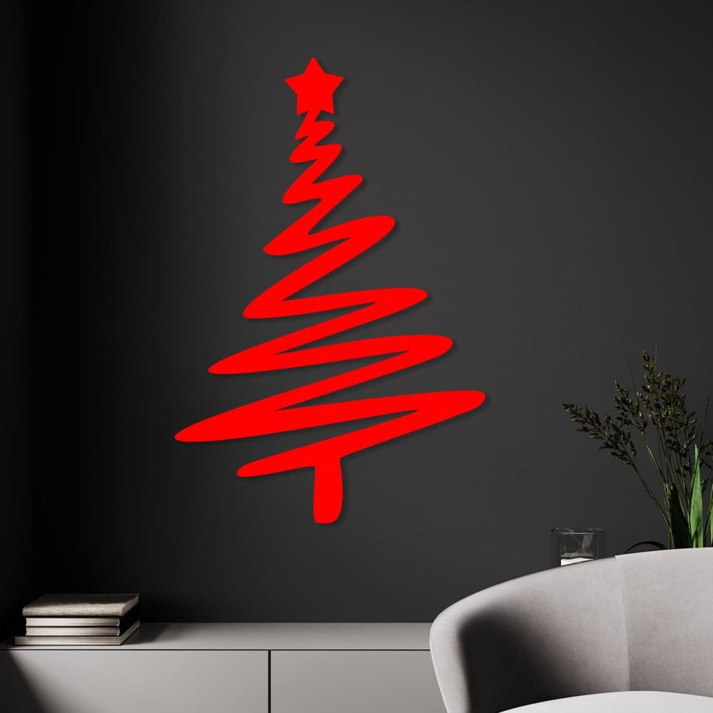 Red Christmas tree-shaped metal wall art with a star on top, mounted on a dark wall above a minimalist white cabinet, with a modern gray chair and greenery in the foreground.