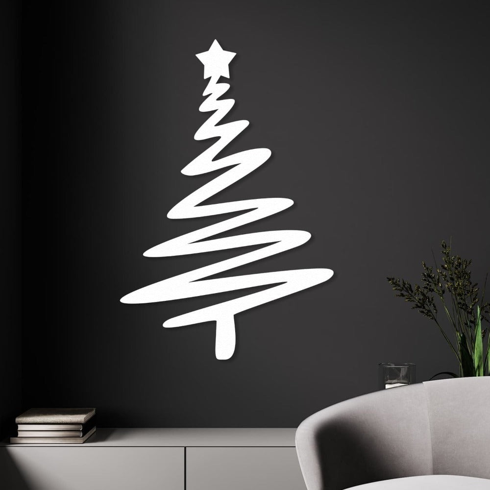 White Christmas tree-shaped metal wall art with a star on top, mounted on a dark wall above a minimalist white cabinet, with a modern gray chair and greenery in the foreground.