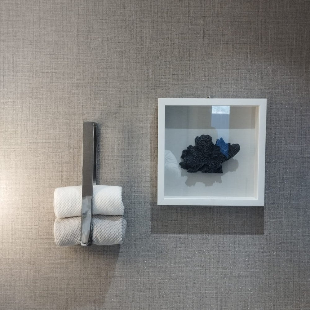 A wall-mounted chrome towel holder with two rolled white and beige towels displayed against a textured gray wall