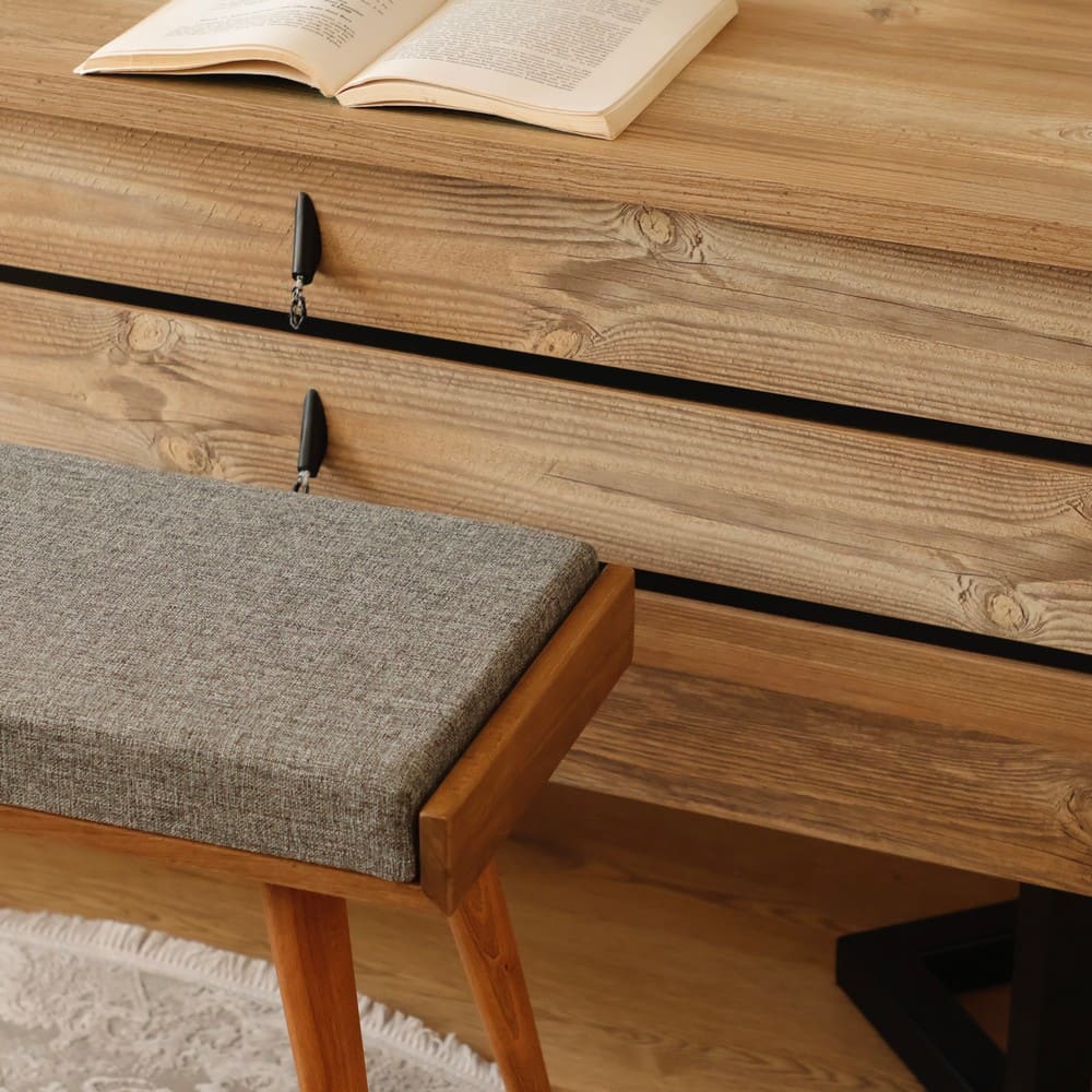 Close-up of a wooden stool with a gray upholstered seat, showing fine craftsmanship and detailing against a wooden cabinet backdrop.