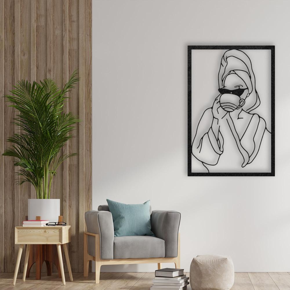 Framed metal wall art of a woman drinking coffee, mounted on a white wall beside a modern armchair with a blue cushion, a small wooden side table, and a tall green plant, creating a cozy corner.