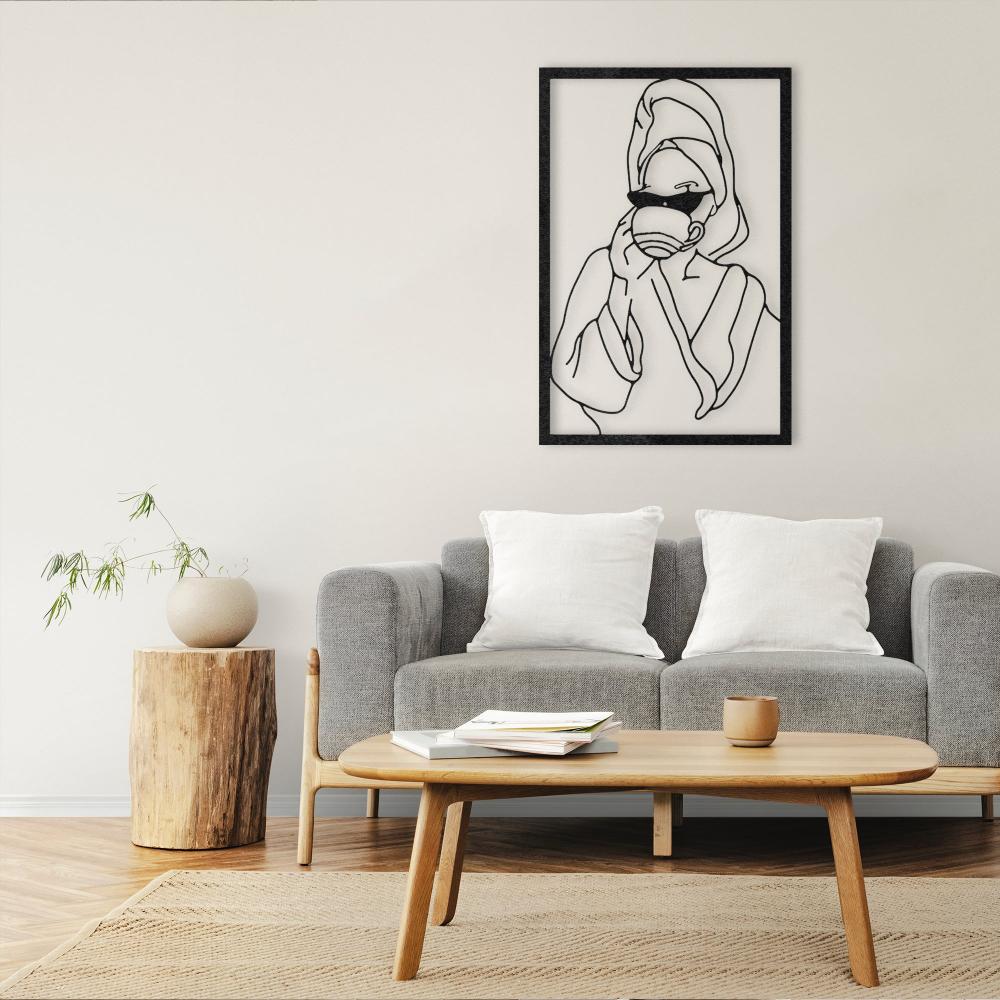 Minimalistic metal wall art depicting a woman sipping coffee, framed and mounted above a modern gray sofa in a neutral living room with wooden and natural decor elements.