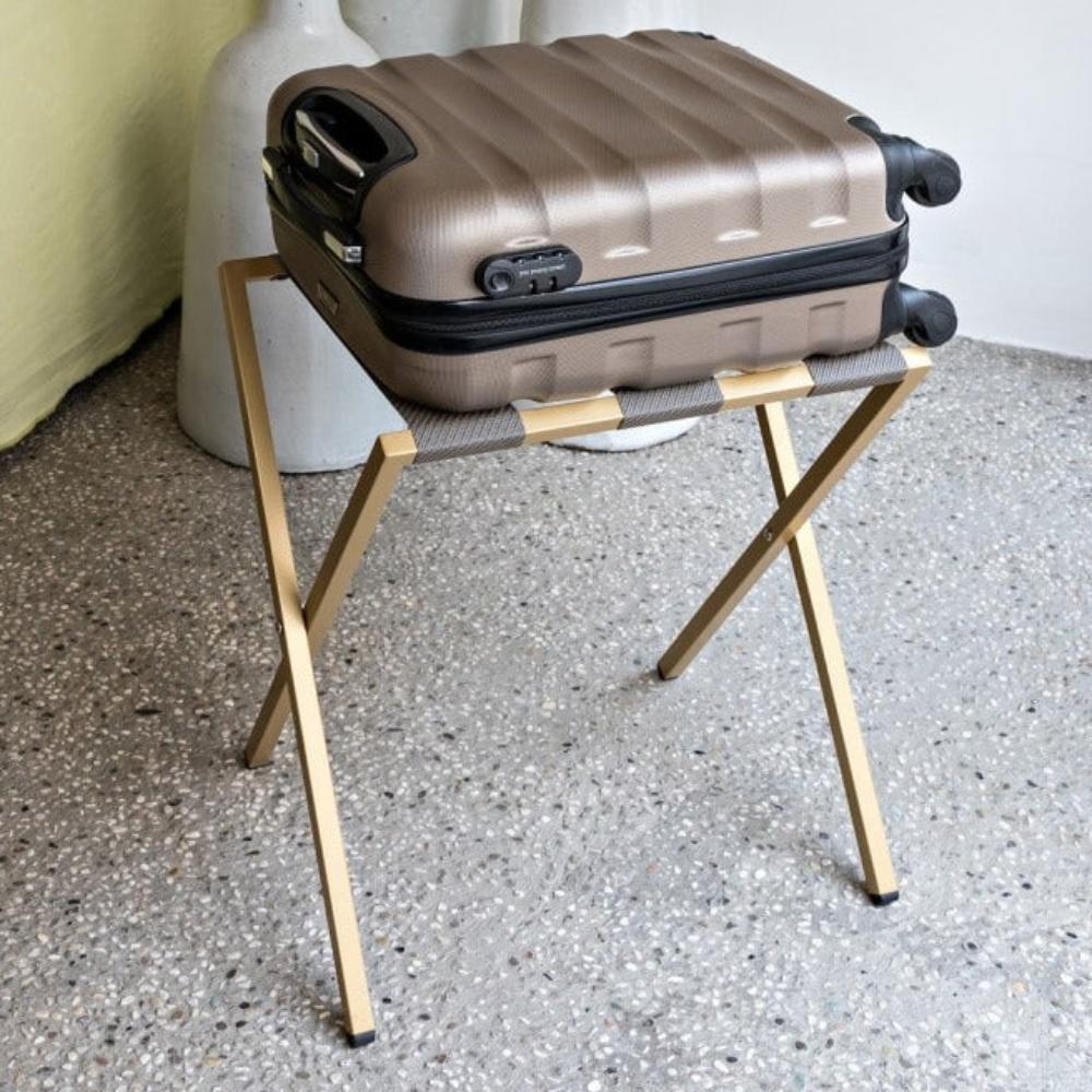 A compact gold foldable luggage rack with a brown suitcase placed on top, demonstrating its functionality and modern design