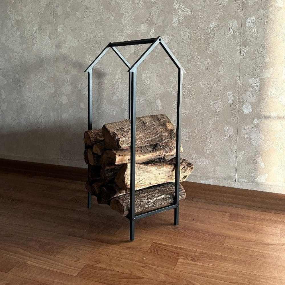 Compact metal firewood rack in a minimalist house-shaped design, neatly stacked with logs, displayed on a warm wooden floor with a textured wall backdrop.