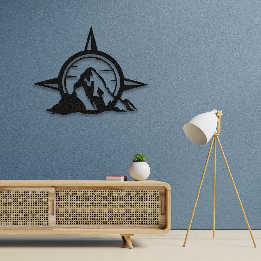 Compass and mountain metal wall art mounted on a light blue wall above a wooden sideboard with a rattan design and a modern lamp.