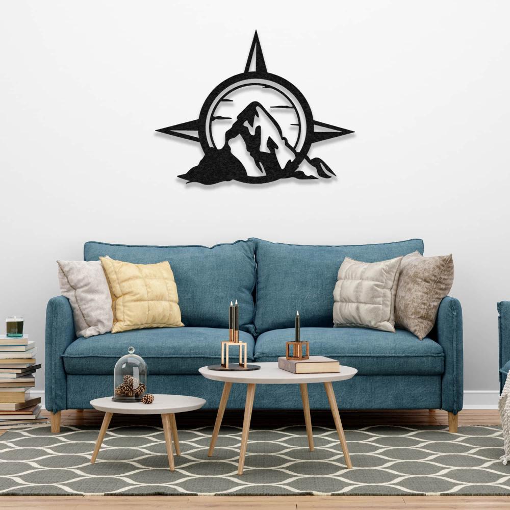 Compass and mountain metal wall art displayed above a blue sofa in a cozy living room with layered coffee tables and books.