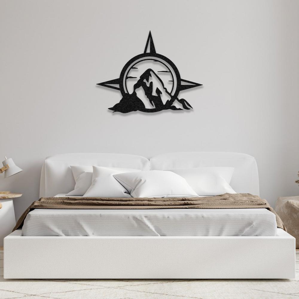 A compass and mountain design metal wall art mounted above a white bed with brown bedding in a simple, elegant bedroom.