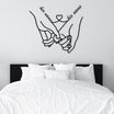 Personalized metal wall decor featuring two holding hands with customizable "her name" and "his name" text connected by a heart, elegantly placed above a modern black and white bed.