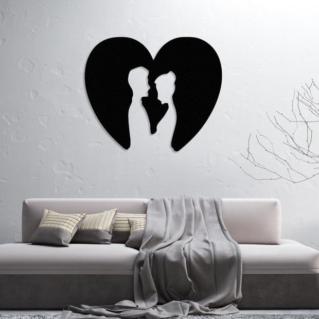 Silhouette-style metal wall art of a couple inside a heart, mounted on a textured white wall above a modern sofa with neutral-colored cushions and a cozy throw.