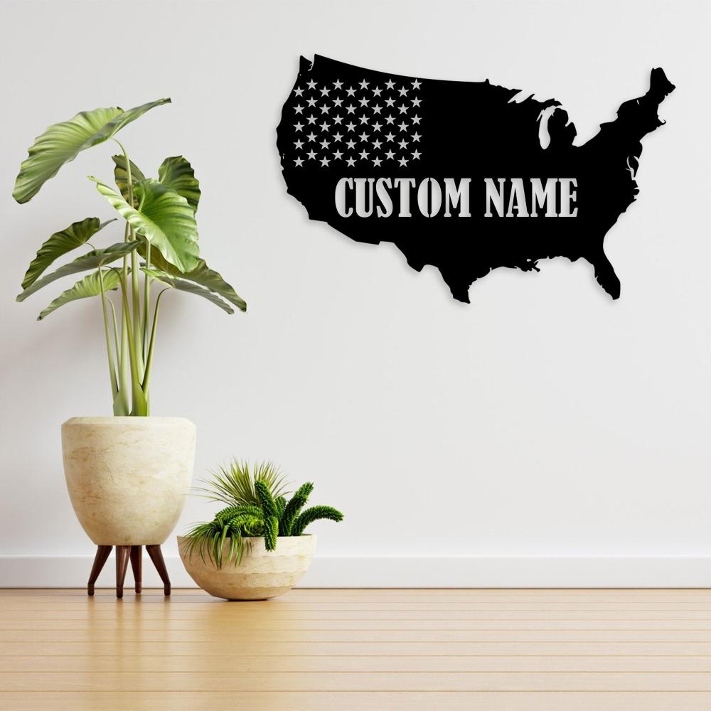 Black metal wall art of the USA map featuring "Custom Name," paired with a modern arrangement of indoor plants in a bright, clean space.