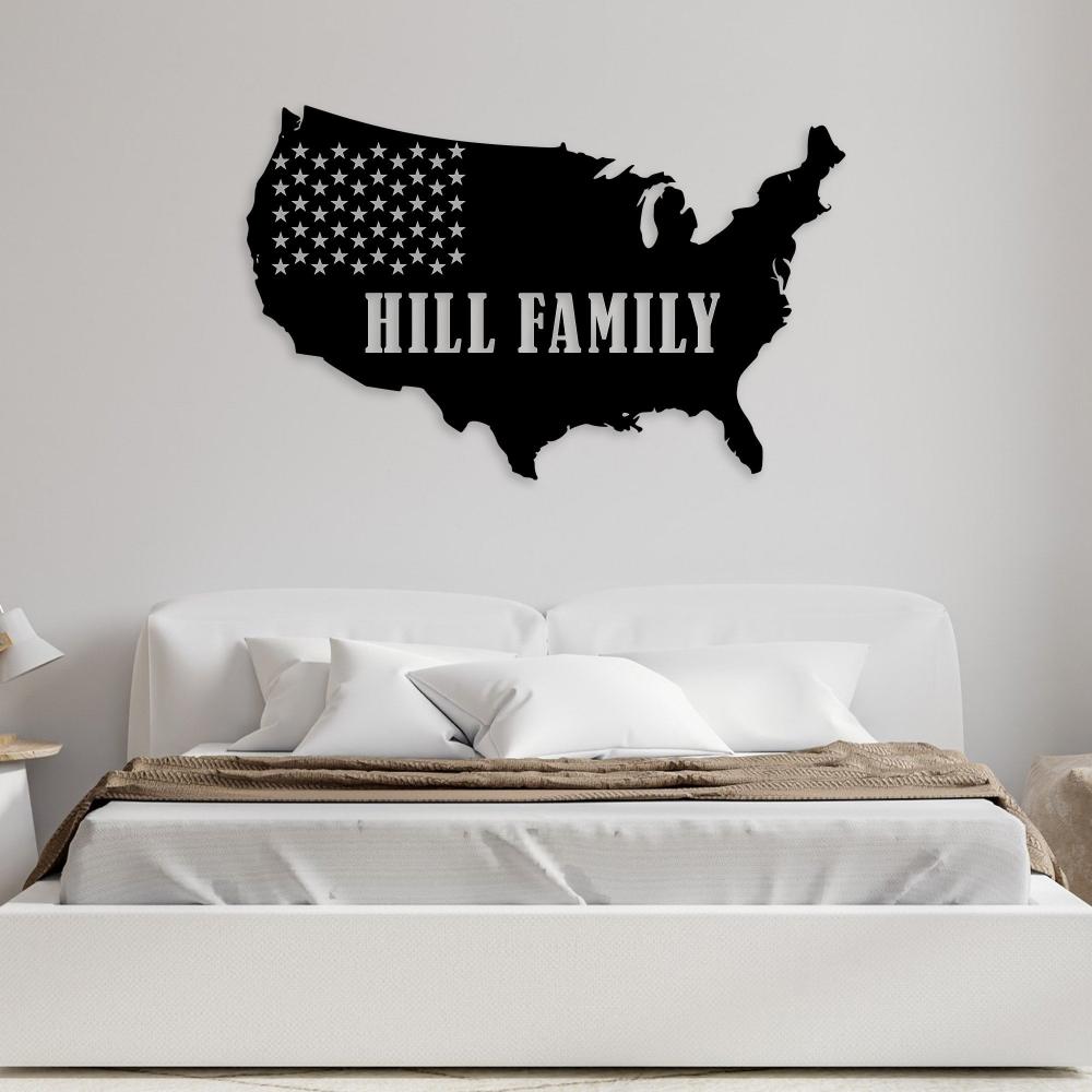 A black metal wall art of the United States map with the text "Hill Family" displayed above a minimalist bed with neutral bedding.