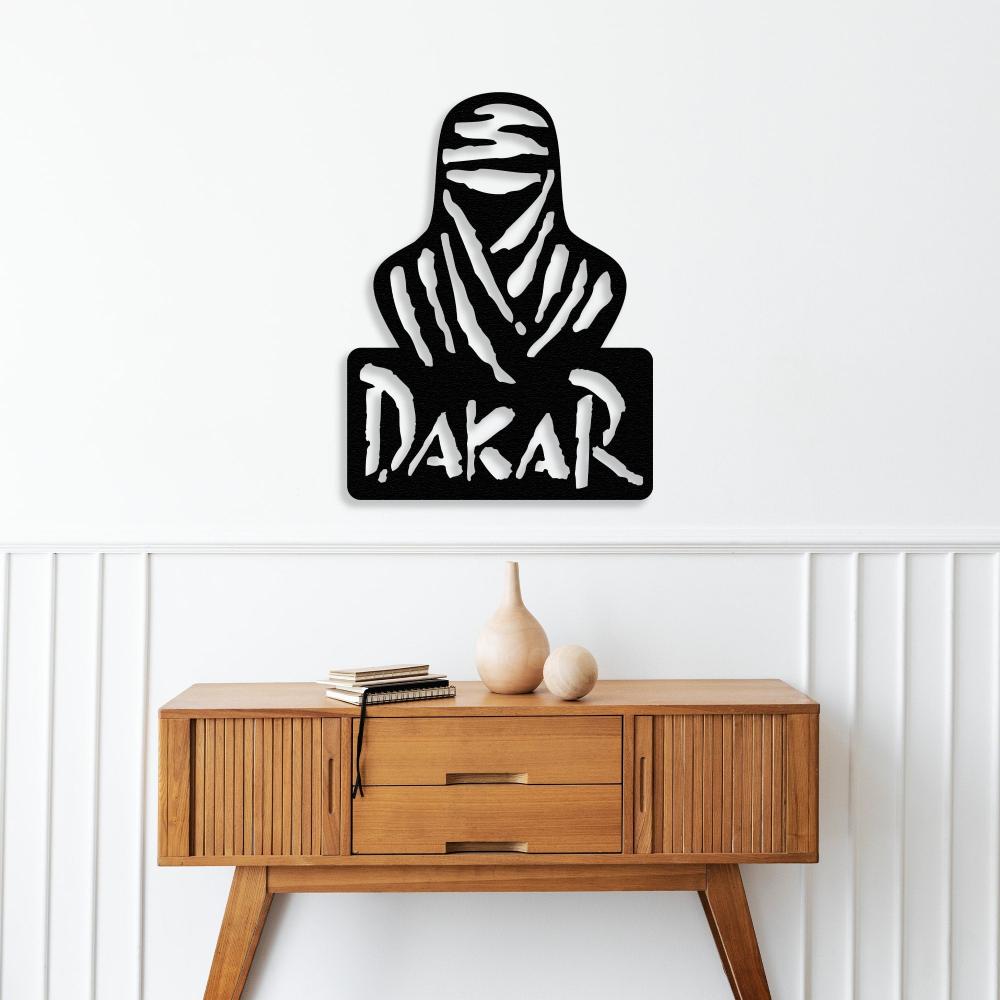 Black Dakar Rally metal wall art showcasing a nomad silhouette and bold "Dakar" text, mounted above a mid-century modern wooden console table. The table features minimalist decor, including two books and a pair of neutral-toned ceramic vases, set against a white paneled wall.