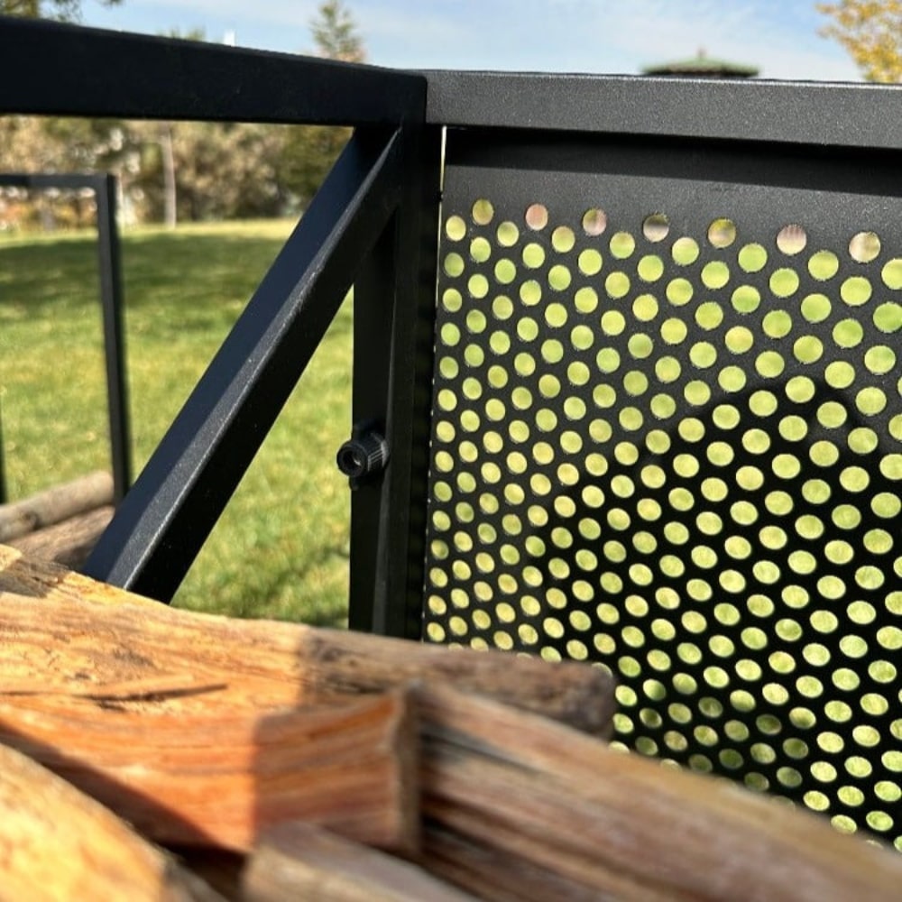 Close-up detail of a black metal firewood holder's mesh backing, highlighting its perforated design and sturdy construction