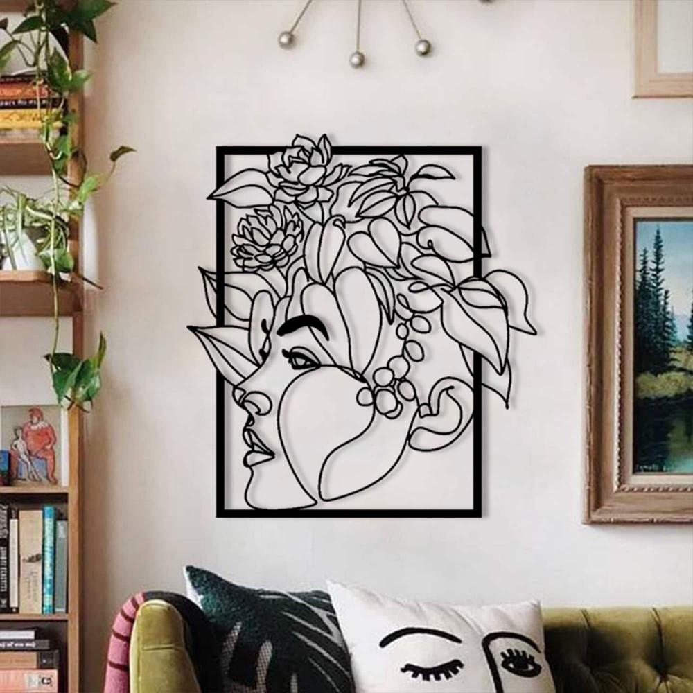 A minimalist metal wall art of a woman's face surrounded by intricate floral elements, displayed on a living room wall with green and pink decor accents.