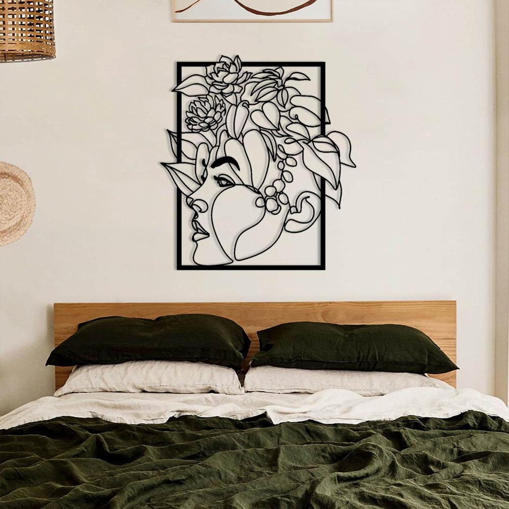 Modern minimalist metal wall art of a woman's face with flowers, elegantly mounted above a bed with dark green bedding in a neutral-toned bedroom.