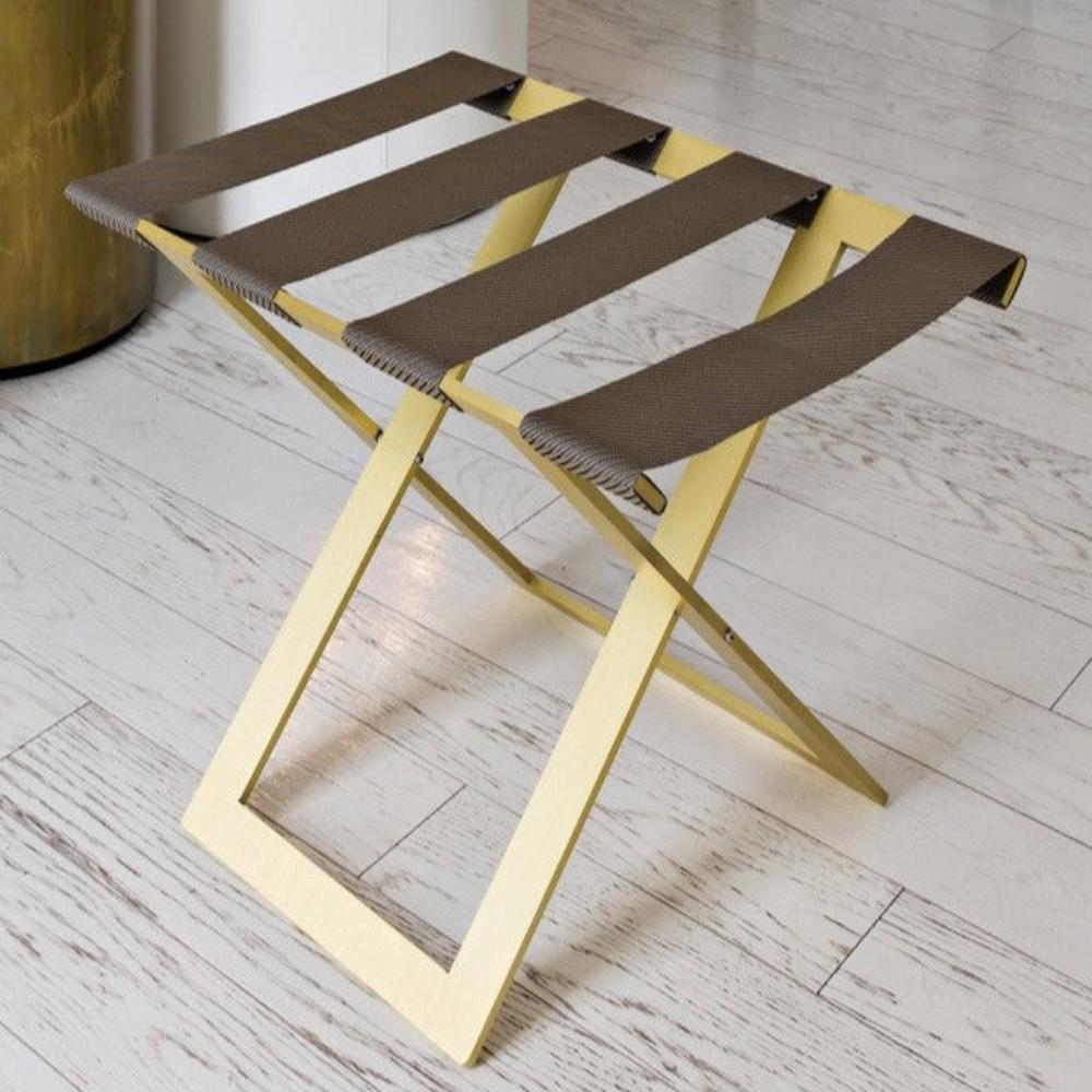 A stylish gold metal luggage rack with genuine leather straps, placed on a light wooden floor, showcasing its elegant design and sturdy structure.